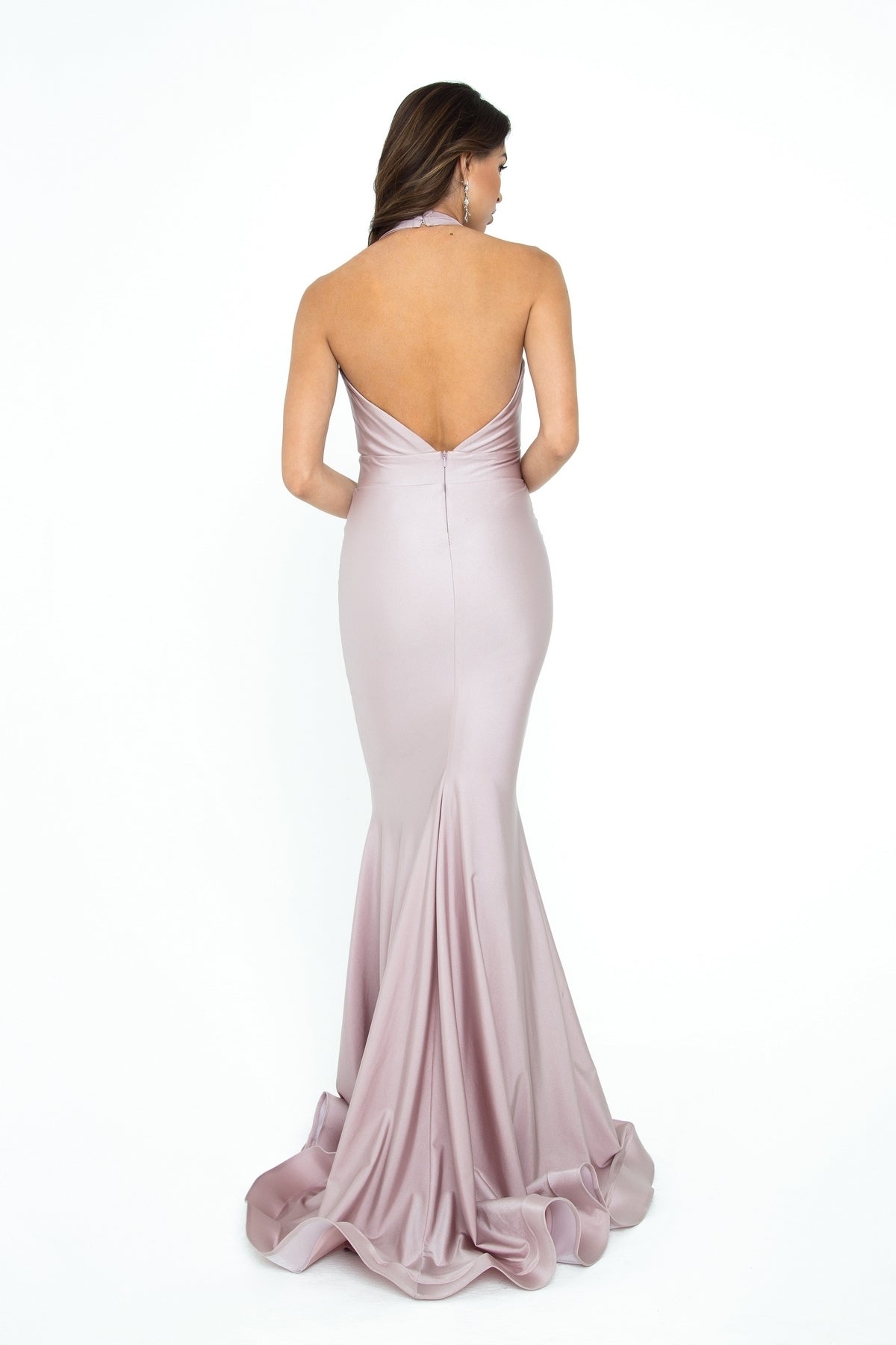A woman stands facing away against a white background, wearing the Deep V-Neck Long Halter Prom Dress: Atria 6202H, a backless, floor-length evening gown in light mauve with a mermaid skirt.